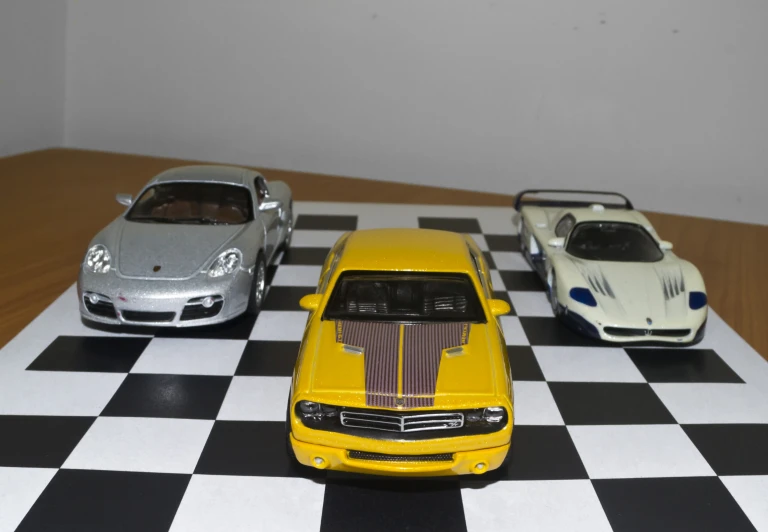 three models of cars sit on a checkered table