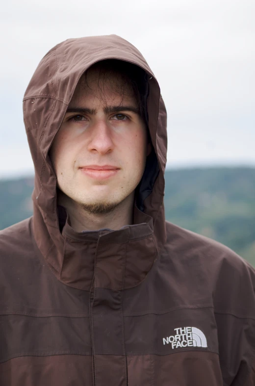 young man wearing brown jacket in outdoors setting