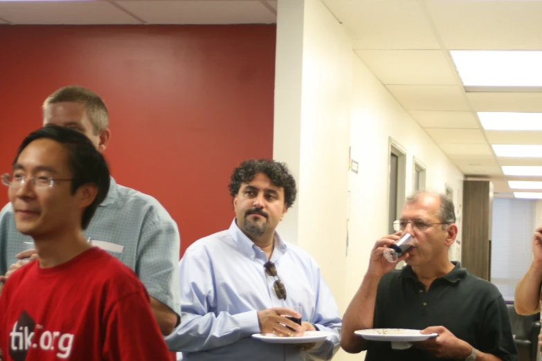 men are standing in a hallway eating from a plate