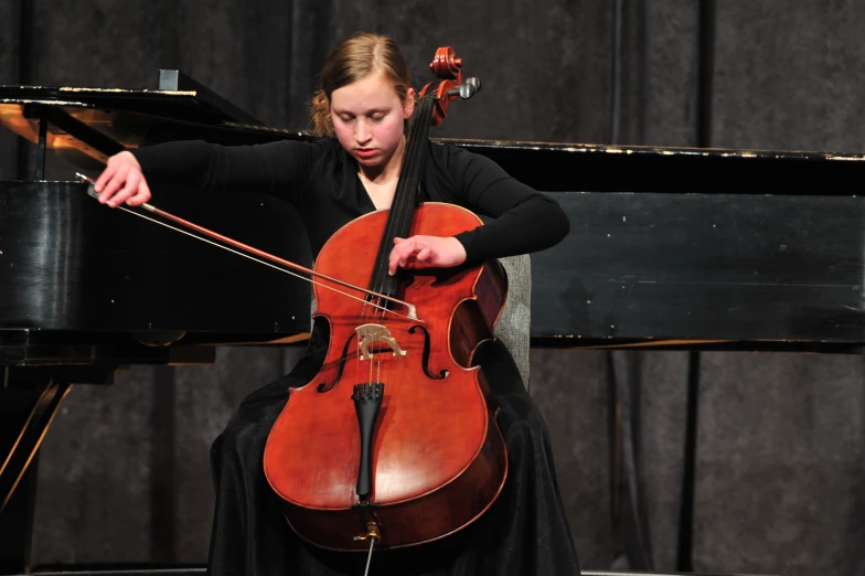 young woman playing cello in front of piano