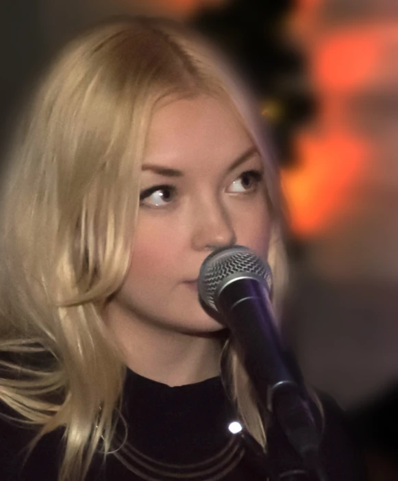 the young woman sings into a microphone while wearing a black dress