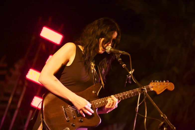 woman with an electric guitar and sunglasses singing into a microphone