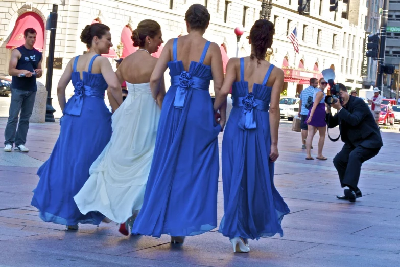 three woman in long blue dresses walk down the street