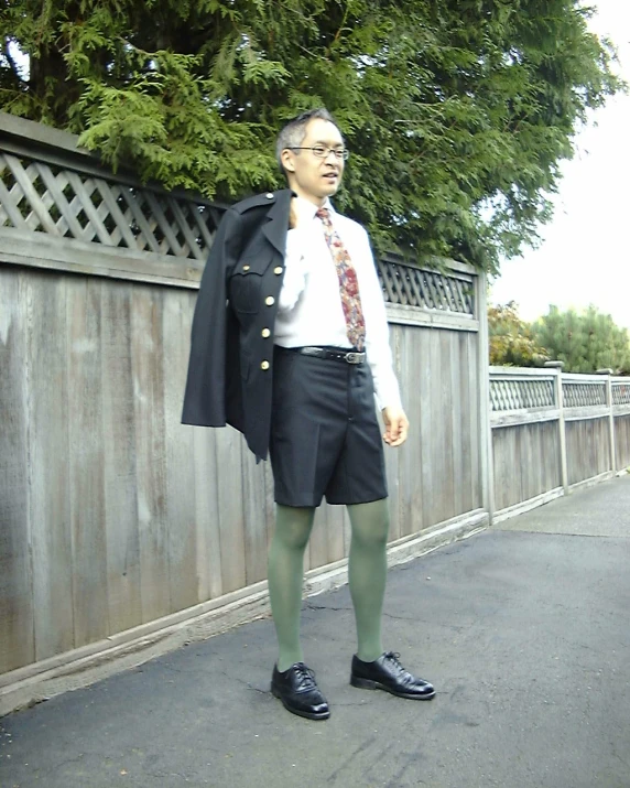 a man in green socks, tie and coat standing near fence