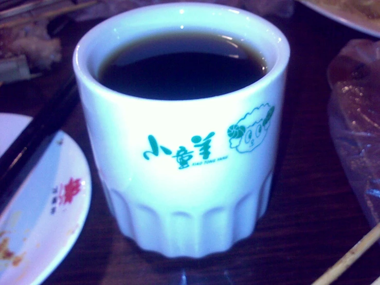 a cup of coffee sits on the table next to a plate and chopsticks