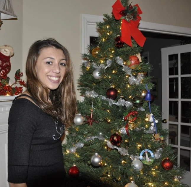 a girl stands beside a christmas tree with red bows