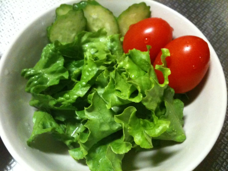 two tomatoes, lettuce and cucumbers in a white bowl