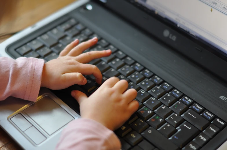 baby in pink holding up the keyboard of a laptop