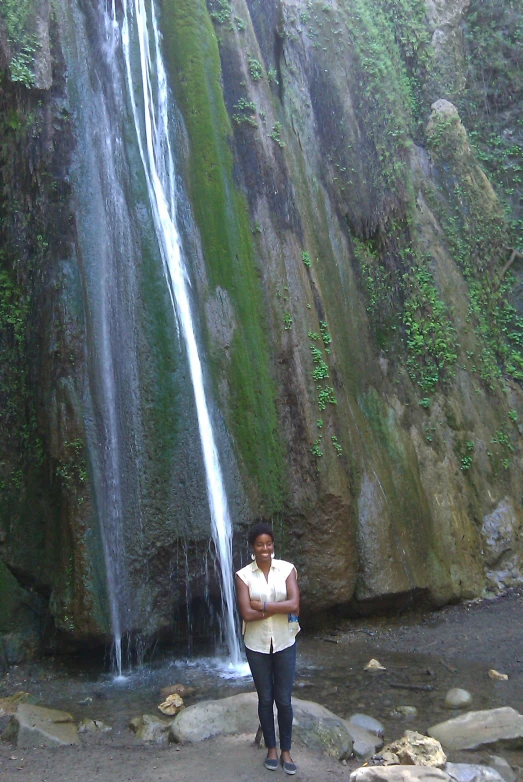 a woman standing next to a waterfall in the woods