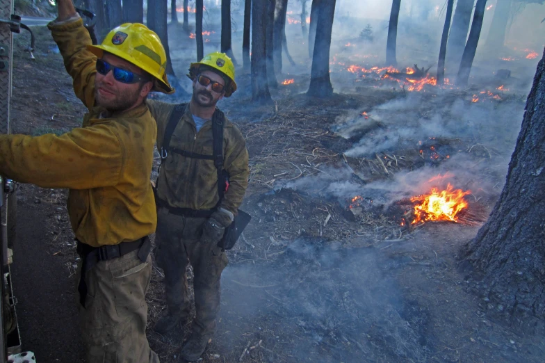 two men wearing helmets look at a bonfire