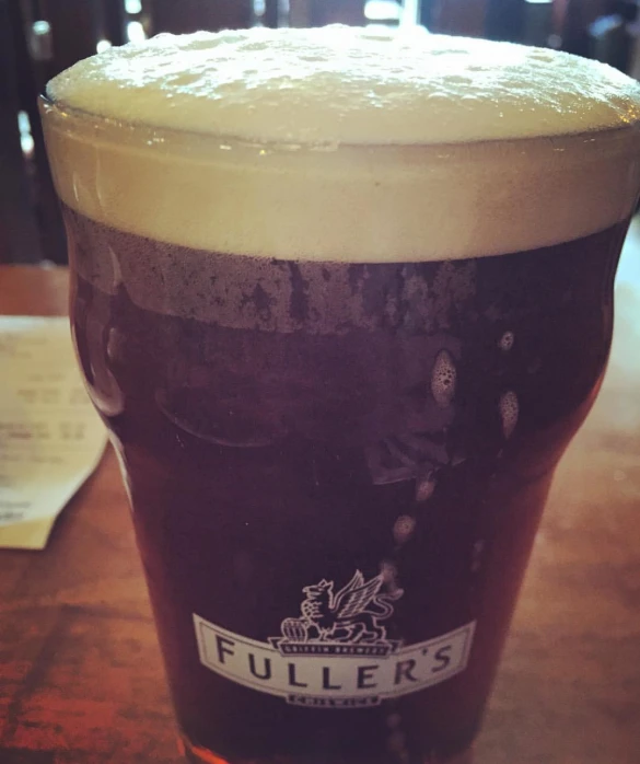 a glass sitting on a table filled with dark beer