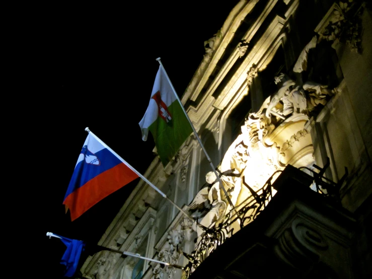 several flags hanging from a building's stone facade at night