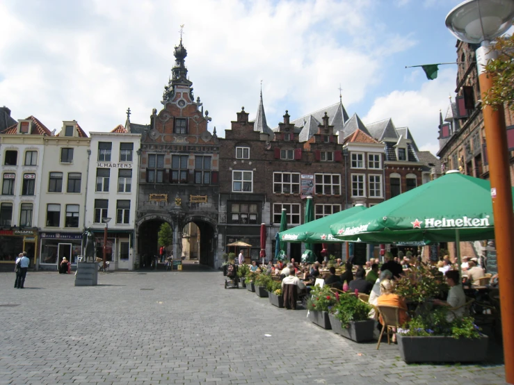 people are sitting and standing near a green umbrella on a cobblestone street