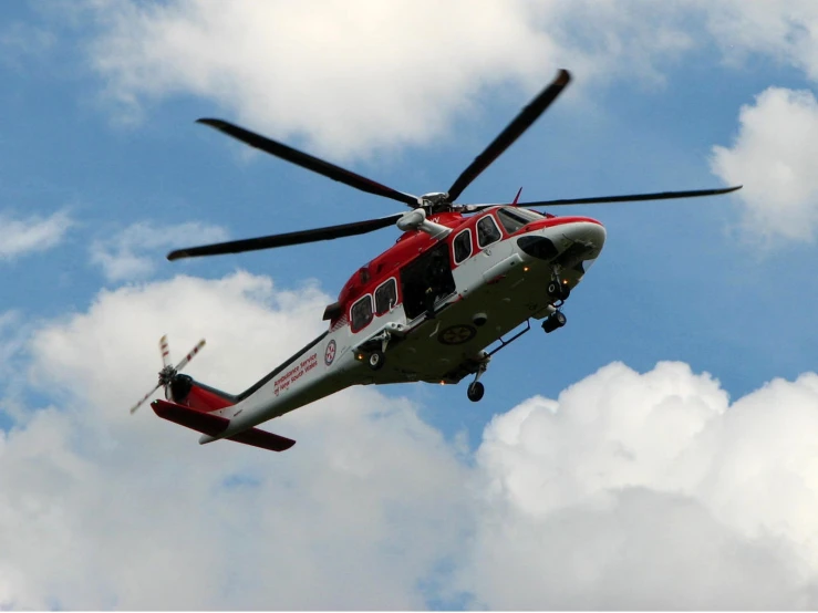 a red and grey helicopter flying through a cloudy sky