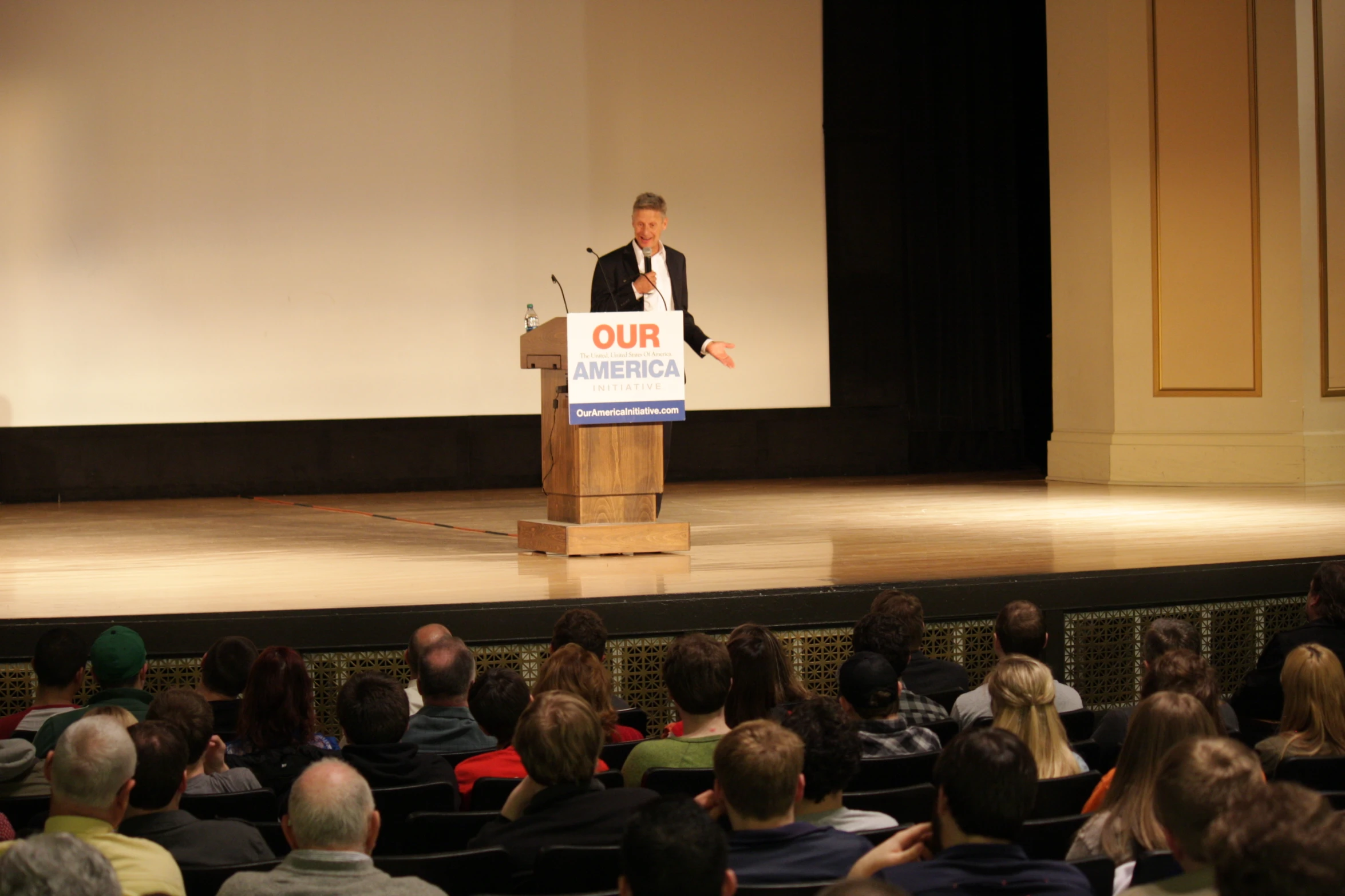 a man is speaking at a podium with people looking on