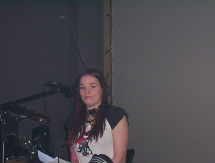 a woman holding her finger up and standing next to a drum