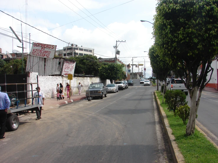 people stand on the curb near cars parked at the edge of the road