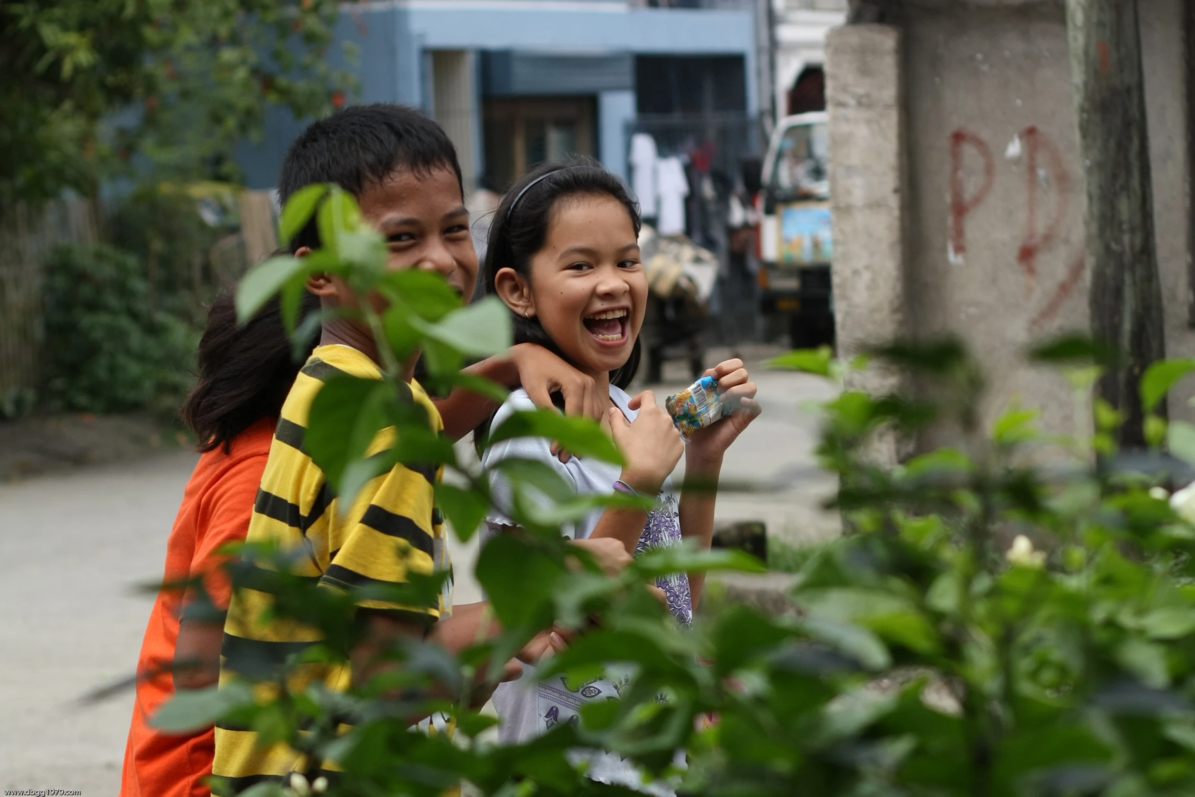 children stand together and laugh next to a building