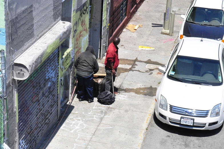 two men standing on a sidewalk next to a wall with graffiti