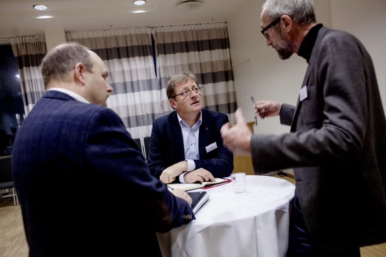 two men stand next to one another at a table