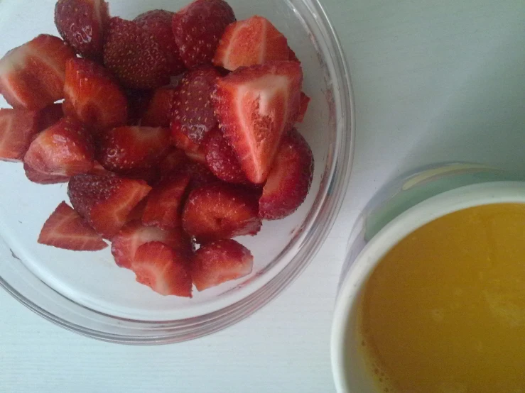 small bowl full of strawberries sitting next to a cup with coffee