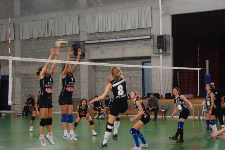 several girls are playing volleyball while one tries to block the ball