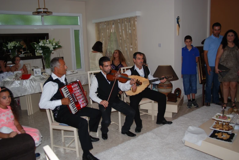 a group of people sit and stand around, while one man plays an instrument in front of other people