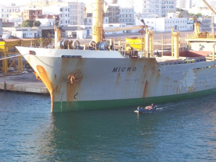 a boat sitting in the water next to a large rusted ship