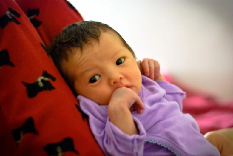 a baby in a purple outfit is hiding against a pillow