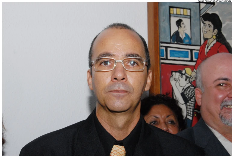 a man with glasses and a black shirt has a picture on the wall