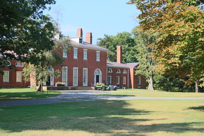 a red brick house with large gardens and trees in front