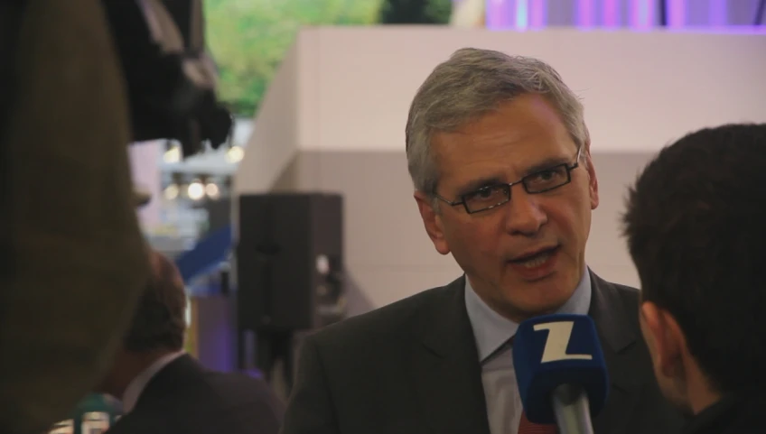 a man with grey hair and glasses wearing a tie and gray jacket talking to other men