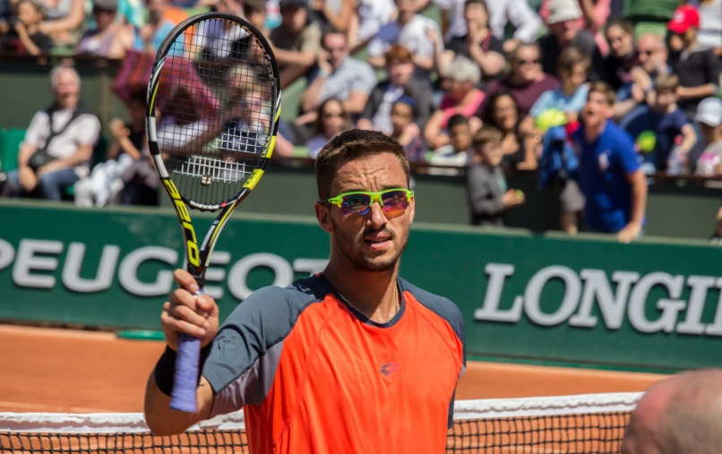 man in orange vest and glasses on tennis court