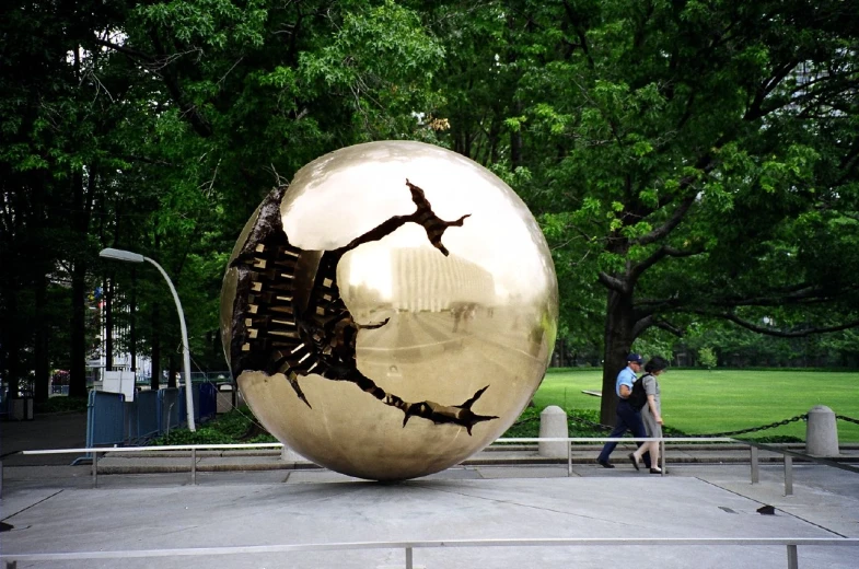 two people walking past a shiny sculpture in a park