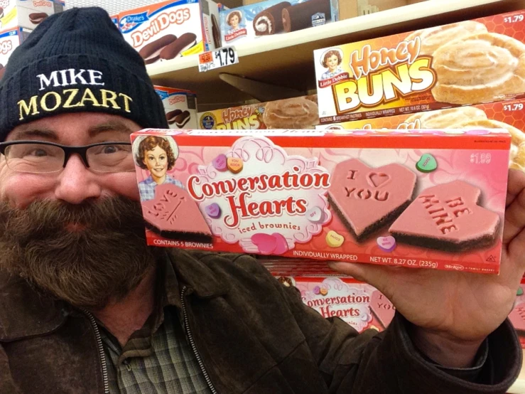 a bearded man in glasses holding up an conversation hearts box