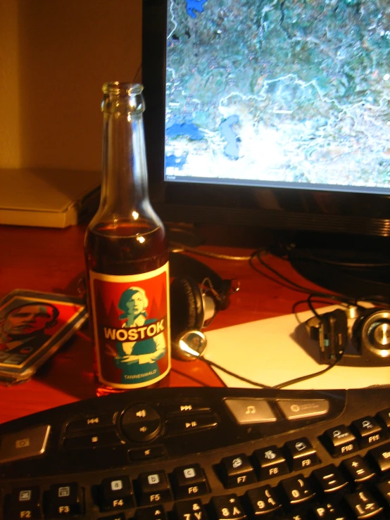 a beer in front of a monitor with headphones on the desk