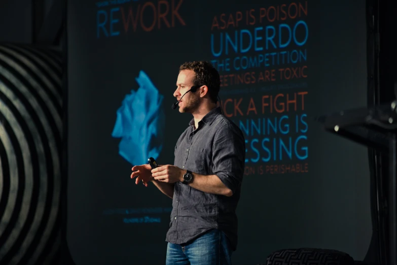 a man in dark shirt standing next to a projector screen