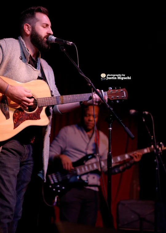 the guitarist is singing into a microphone and guitar while three other people play instruments behind him