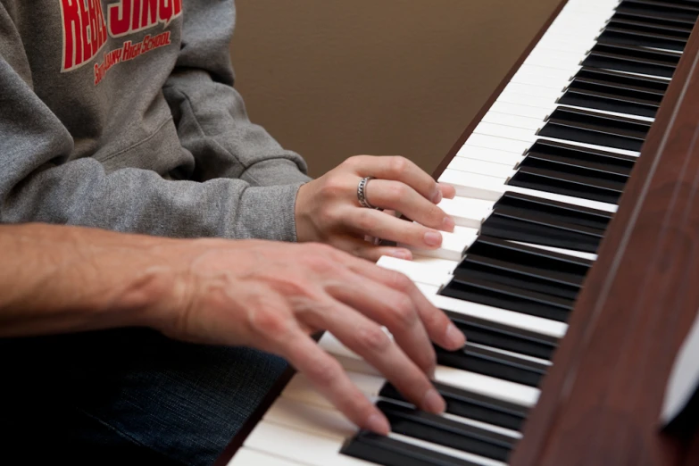 a man in grey sweatshirt playing piano with hands