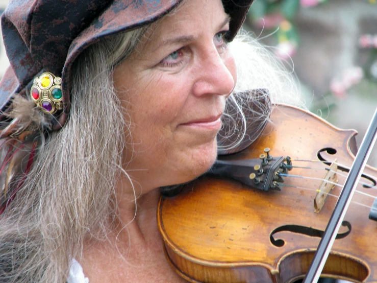 a woman plays her violin while wearing an old hat