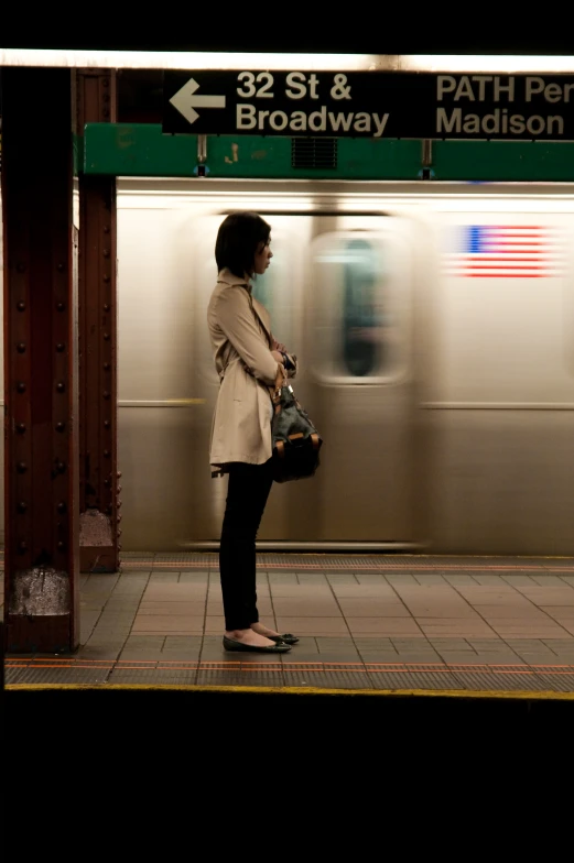 a woman is standing near a subway sign on the platform