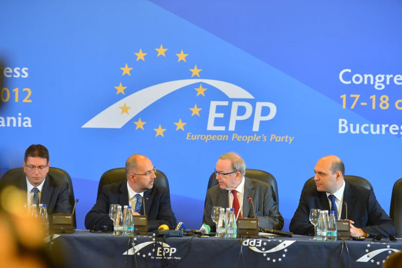 five men sitting down in front of a blue wall and sign