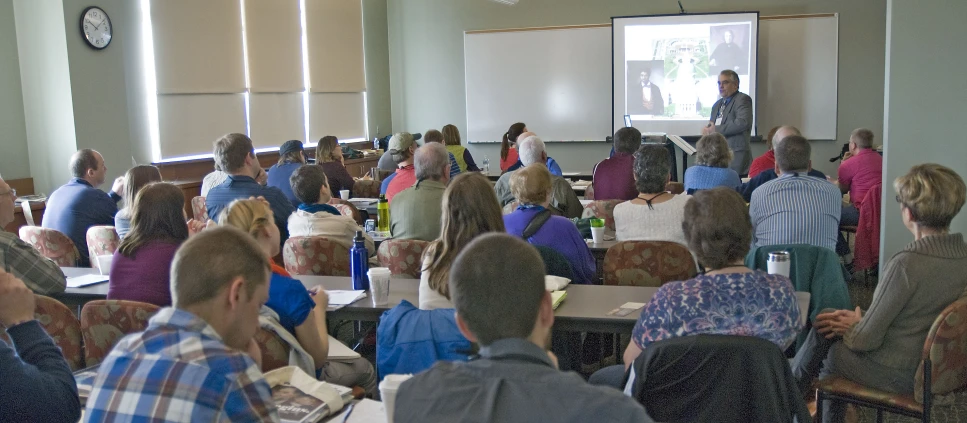 a group of people sitting at tables with one man giving a lecture