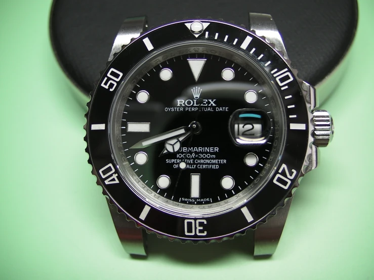 a black rolex watch sitting on a green table