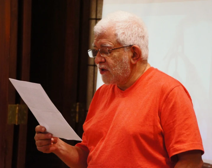 a man in a orange shirt and glasses is holding a piece of paper