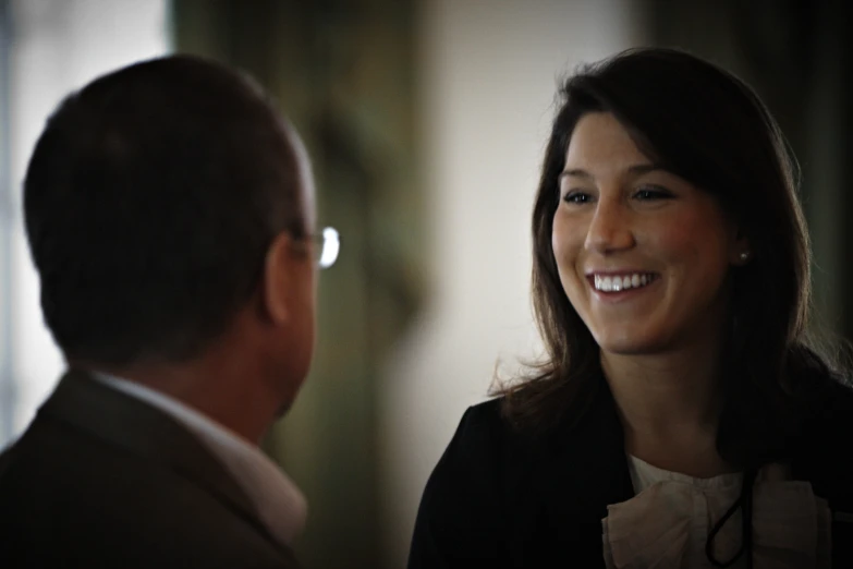 smiling woman with dark brown hair is in front of man wearing a suit