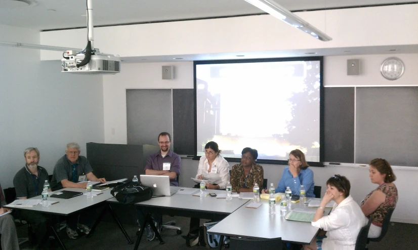 a group of people sitting around a table in front of a projector screen