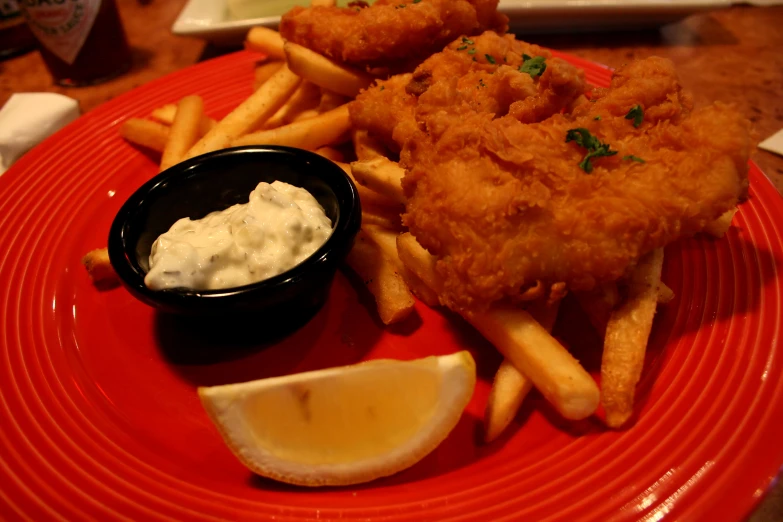 fried fish and french fries on a red plate with some dipping sauce