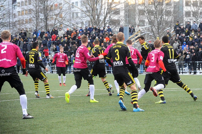 men in black and pink playing soccer in front of a crowd