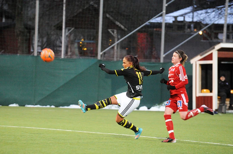 two girls kicking around a soccer ball on a soccer field